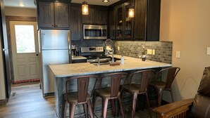 A modern kitchen with dark wood cabinets, stainless steel appliances, a large island with bar stools, and pendant lighting. - Schweitzer true ski in ski out condo (Sandpoint)