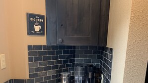 A compact kitchen with dark wooden cabinets, a tiled backsplash, and a countertop with coffee-making equipment. - Schweitzer true ski in ski out condo (Sandpoint)