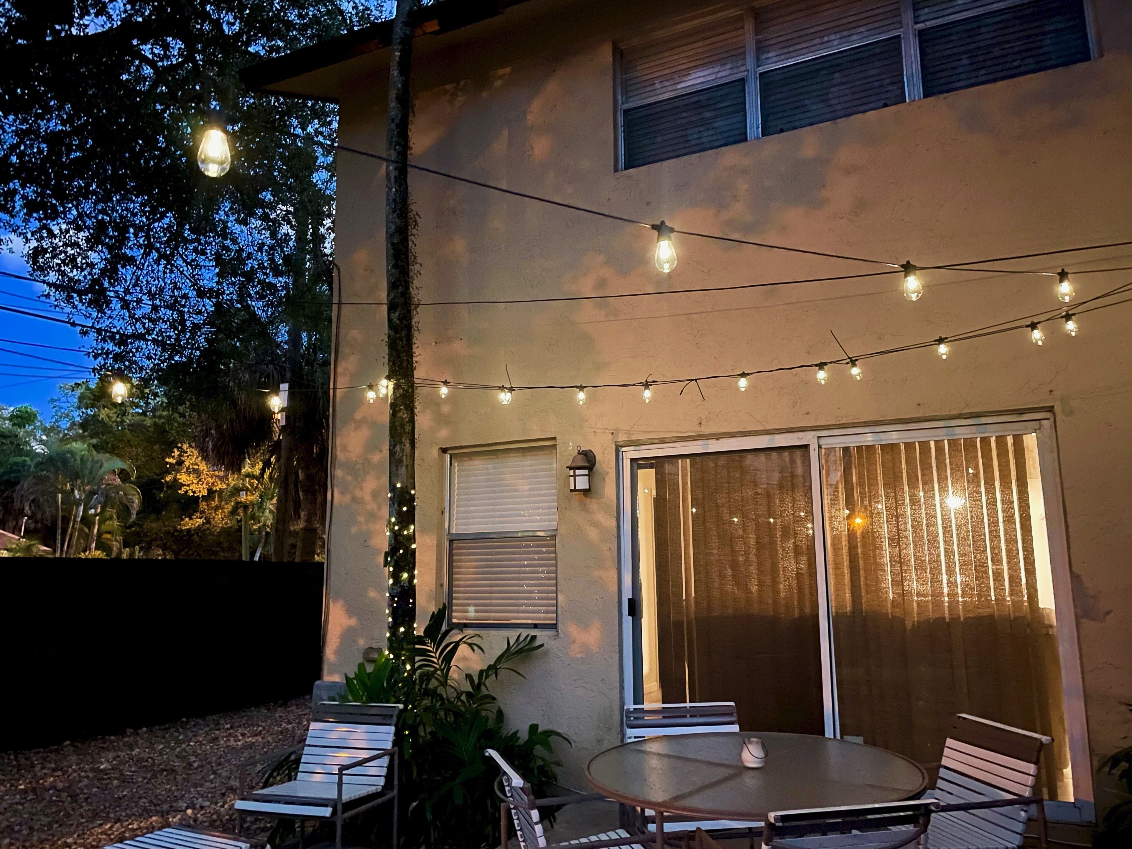 Patio esterno con tavolo e sedie rotonde, luci a stringa e una porta scorrevole in vetro.