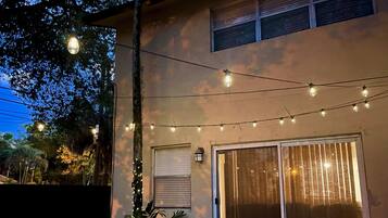 Patio esterno con tavolo e sedie rotonde, luci a stringa e una porta scorrevole in vetro.