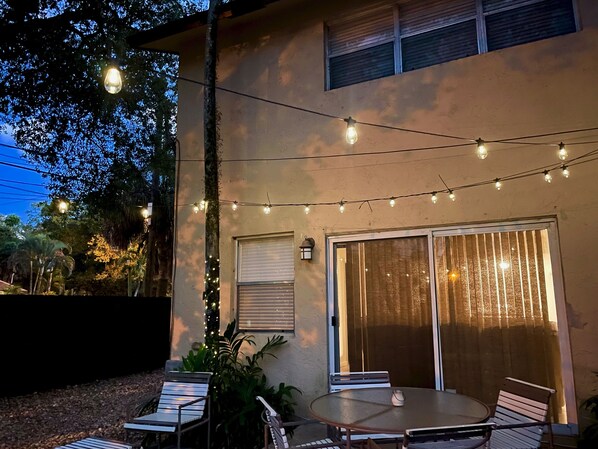 An outdoor patio with a round table and chairs, string lights, and a sliding glass door.