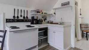 A compact kitchen with white cabinets, a stove, and a microwave. There are utensils hanging on the wall and a coffee maker on the counter.