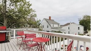 A deck with red chairs and a table, overlooking a white house with a gray roof.