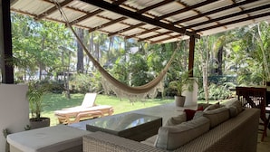 A covered outdoor seating area with wicker furniture, a hammock, and a view of a lush garden. - Beachfront  3-Bedroom Home in Santa Teresa with AC  (Santa Teresa, Mal Pais)
