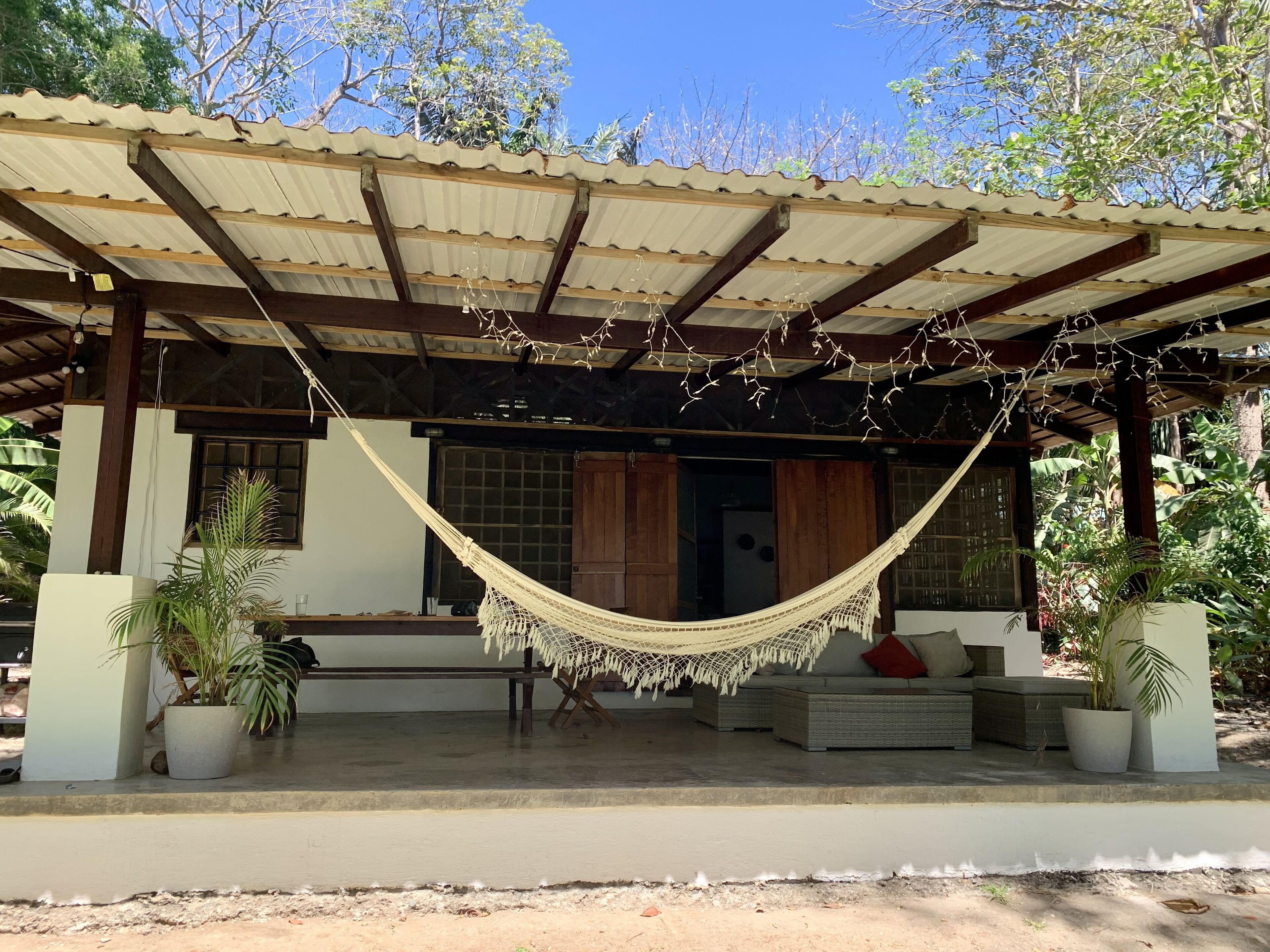 A covered outdoor seating area with a hammock, potted plants, and a wooden bench.