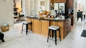 Una cocina amplia con una isla grande, armarios de madera y piso de mármol.