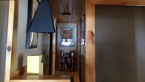 Interior de madera con lámpara colgante, una estantería y una puerta que da a otra habitación.