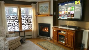 Una sala de estar acogedora con chimenea, un televisor montado en la pared y una alfombra estampada en el suelo.