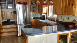 Una cocina con armarios de madera, un refrigerador de acero inoxidable, una encimera de granito y lámparas colgantes.