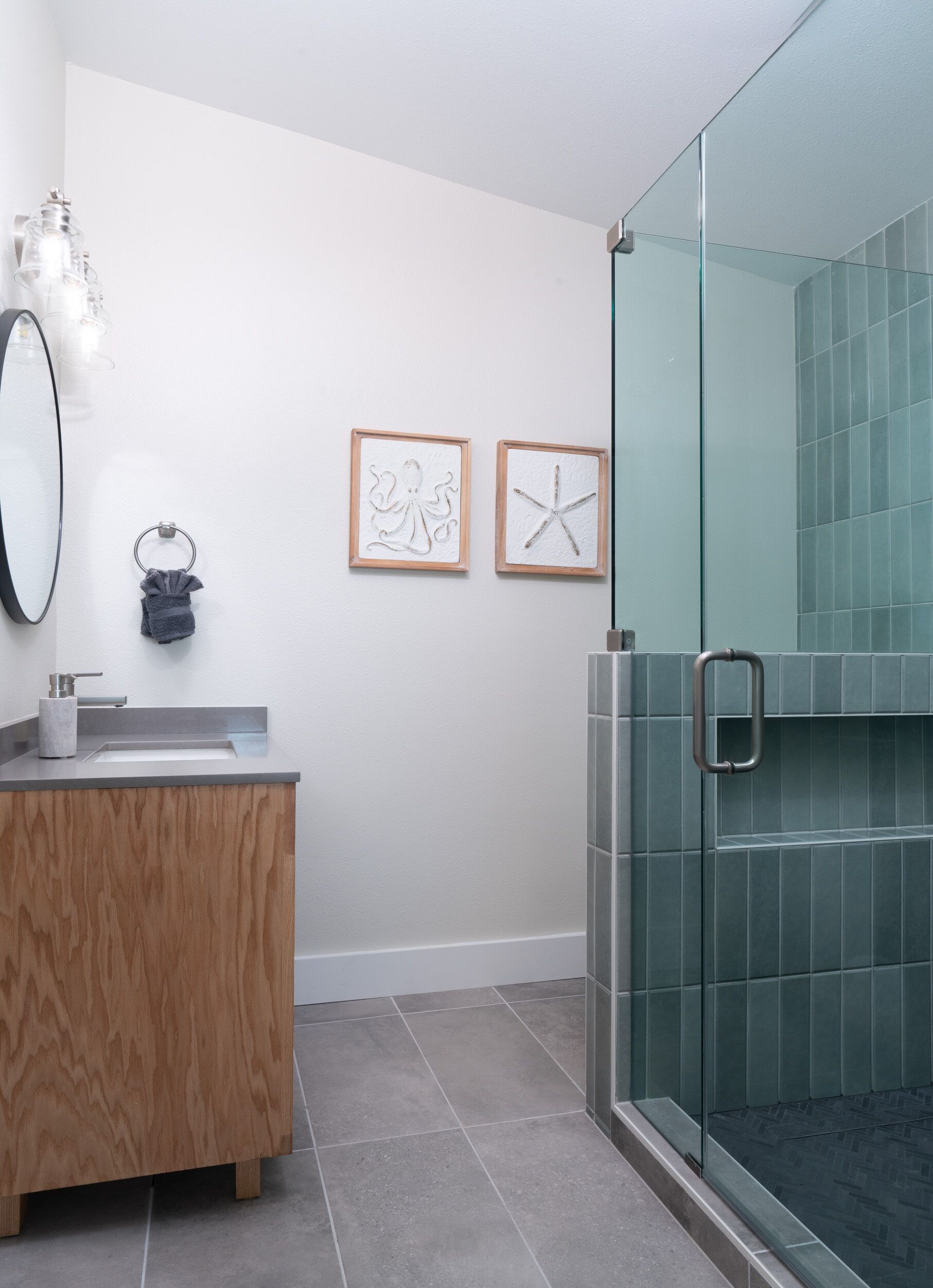 A modern bathroom with a wooden vanity, a glass shower enclosure, and two framed wall art pieces.