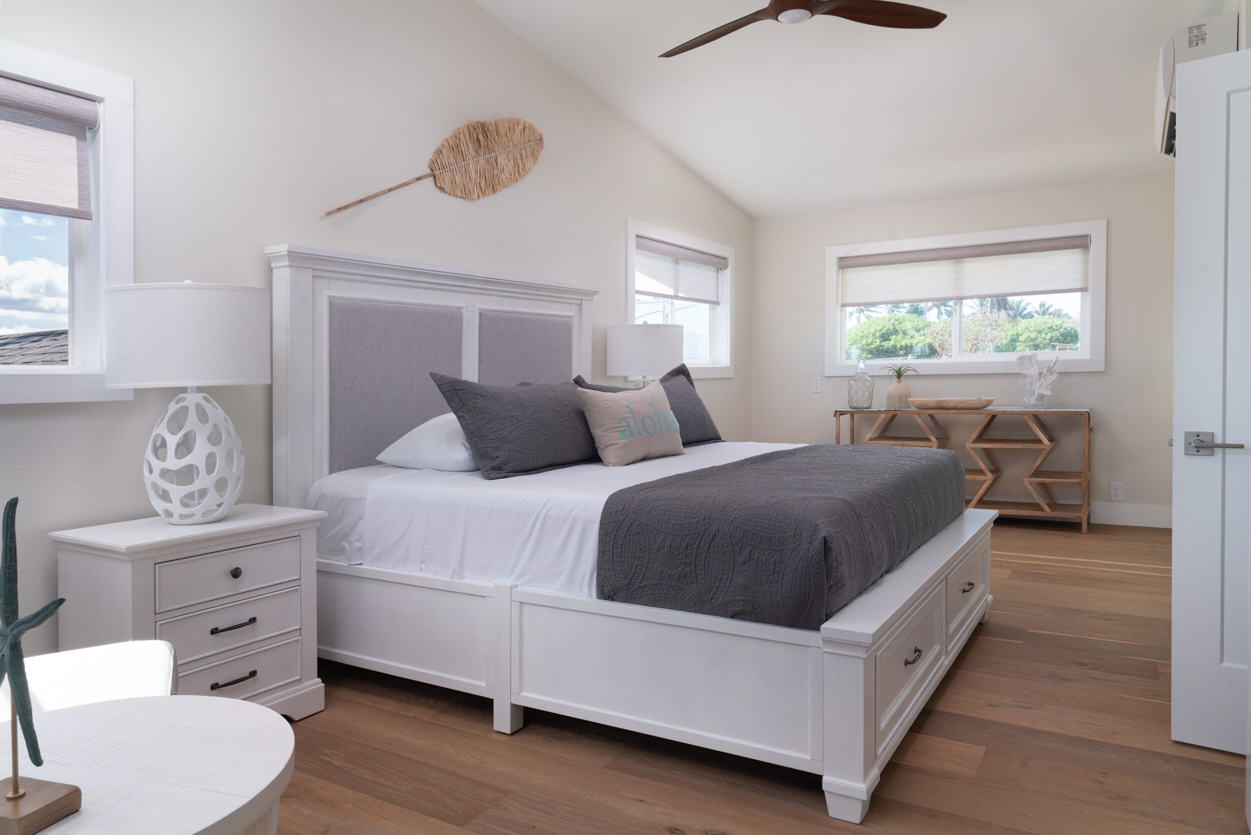 A bedroom with a bed, bedside tables, a ceiling fan, and a window with a view of greenery.