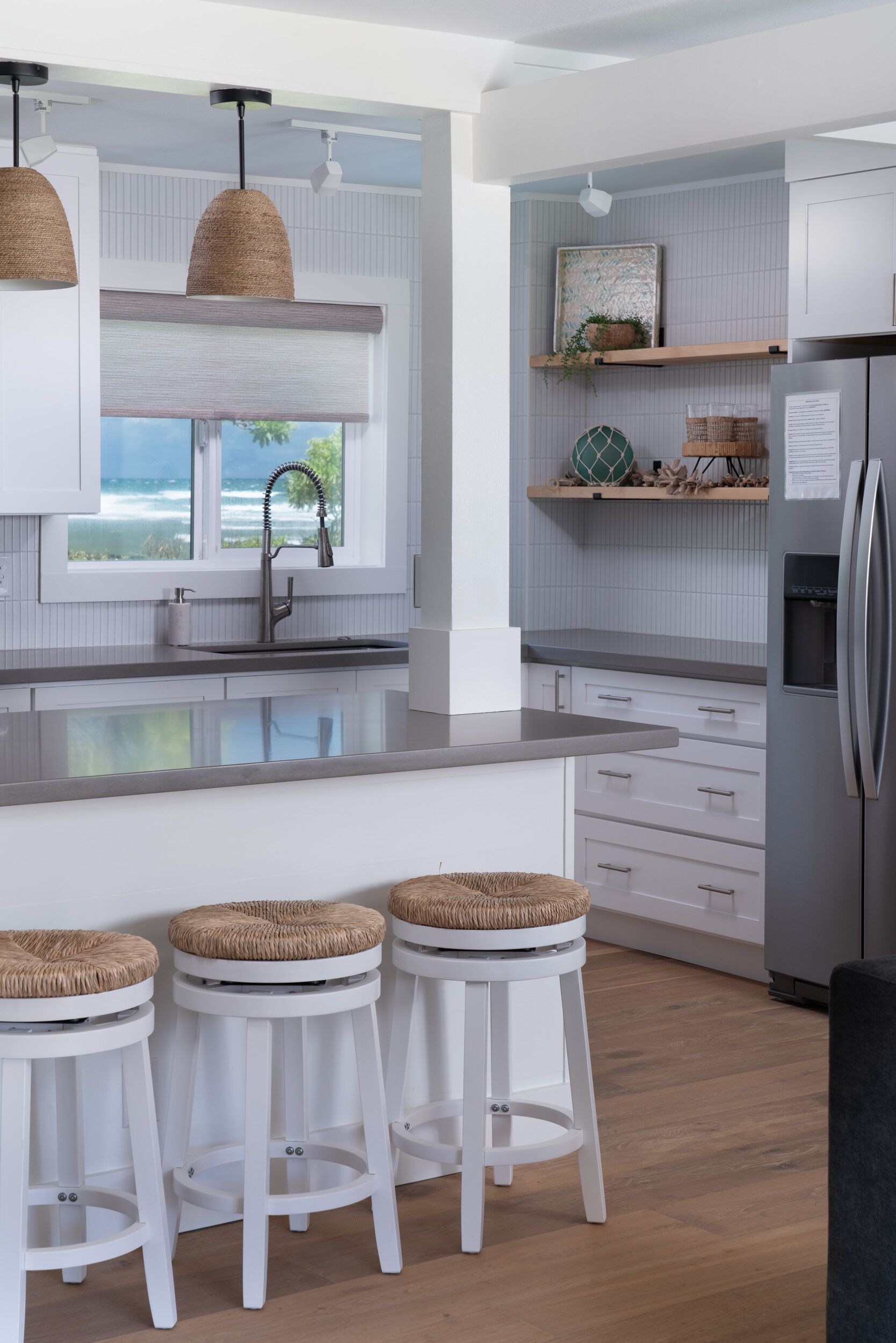 A modern kitchen with white cabinetry, a large window with a view, and three wicker stools.