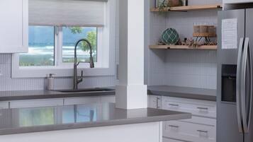 A modern kitchen with white cabinetry, a large window with a view, and three wicker stools.