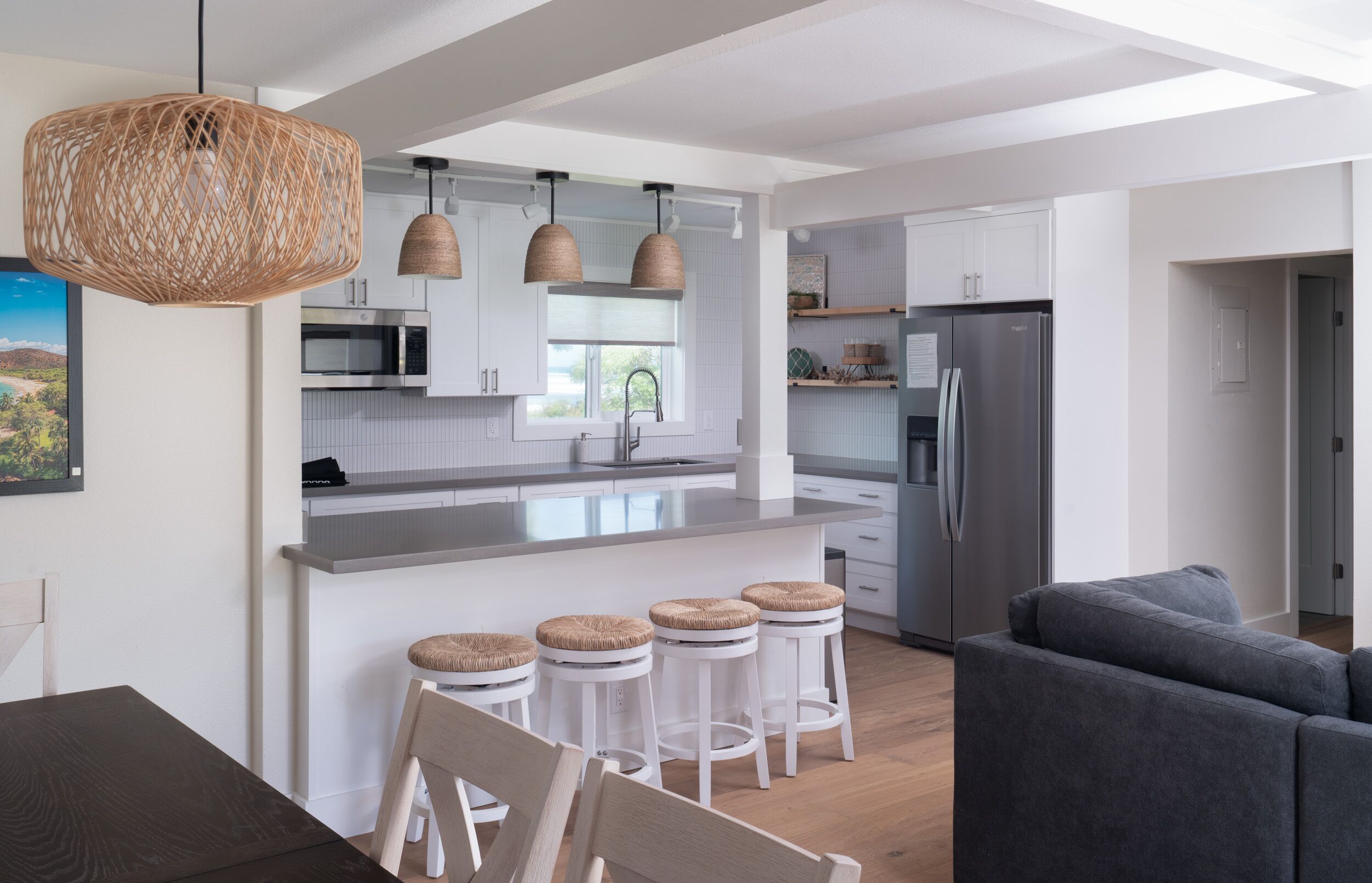 Une cuisine moderne avec des meubles blancs, un îlot central doté de tabourets, un grand réfrigérateur et des luminaires suspendus.