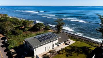A modern house with a solar panel roof, a driveway, and a view of the ocean.