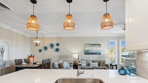Una cocina moderna con una isla grande, pileta de acero inoxidable y lámparas colgantes.