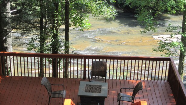 Une terrasse en bois avec deux chaises et une table, donnant sur une rivière.