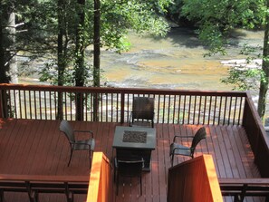 A wooden deck with two chairs and a table, overlooking a river.