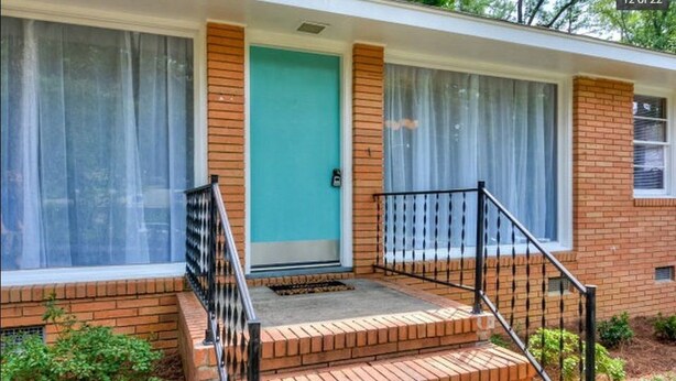 A two-story brick house with a front porch, a blue door, and a small set of steps leading to the entrance. - Mid Century Modern Retreat in North Augusta (North Augusta)