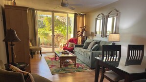 A living room with a sofa, a coffee table, a dining table, and chairs. There is a large window with curtains, a ceiling fan, and a lamp. - SEPTEMBER VALUE Last minute cancelation! A/C, Ocean Views Near Keawakapu Beach! (Kihei)