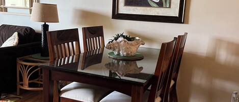 A dining area with a glass-top table, wooden chairs, and a framed floral artwork on the wall.