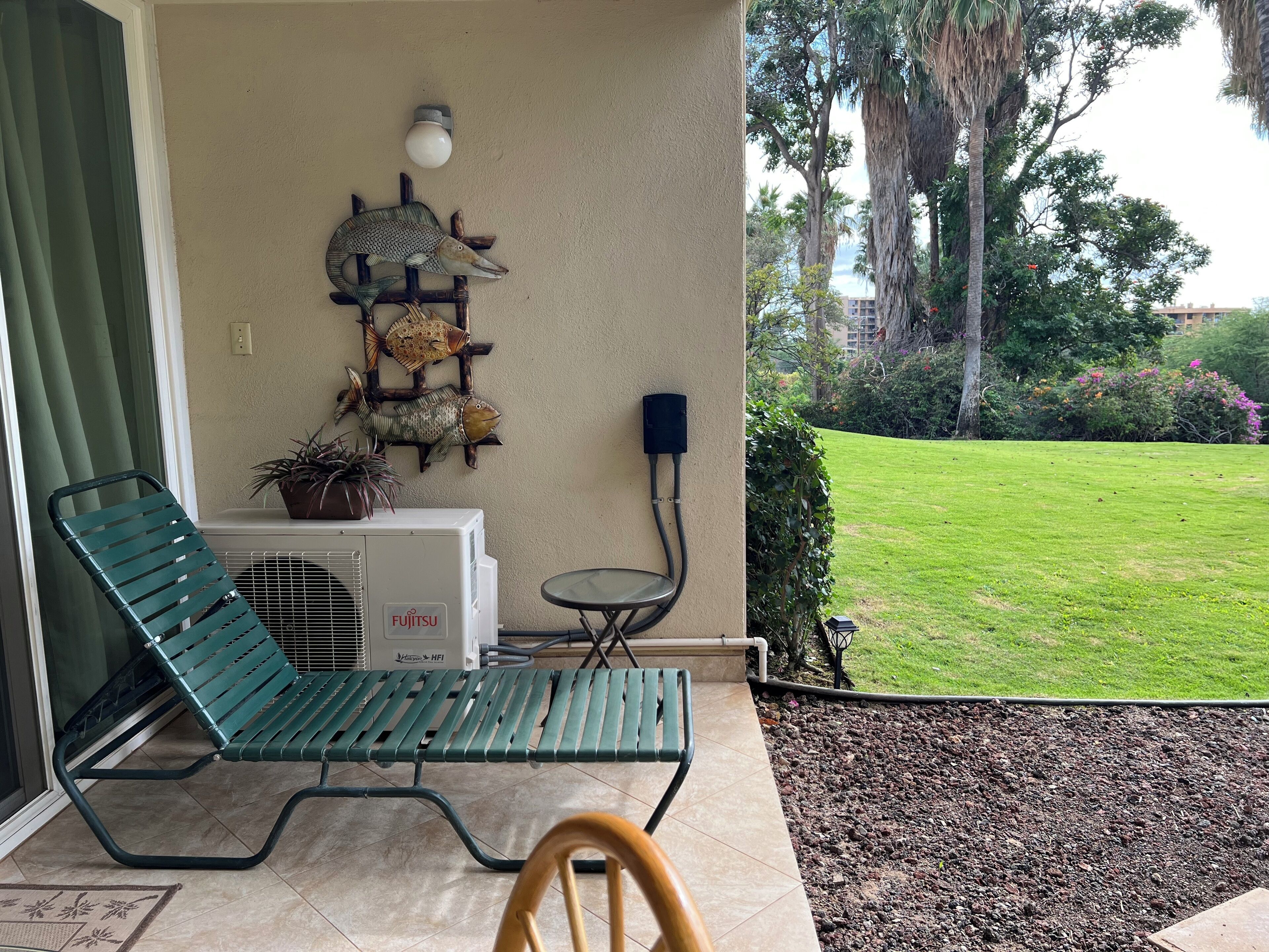 A green lounge chair, a small table, a wall-mounted air conditioner, and a garden view.