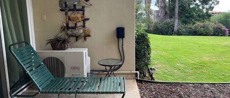 A green lounge chair, a small table, a wall-mounted air conditioner, and a garden view.