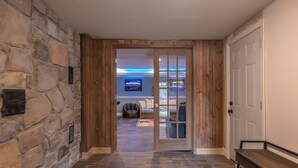 A hallway with stone walls, a wooden bench, and a door leading to a living area with a TV and seating.