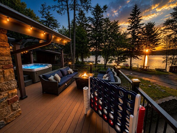A deck with a hot tub, outdoor seating, and a view of a lake at sunset.