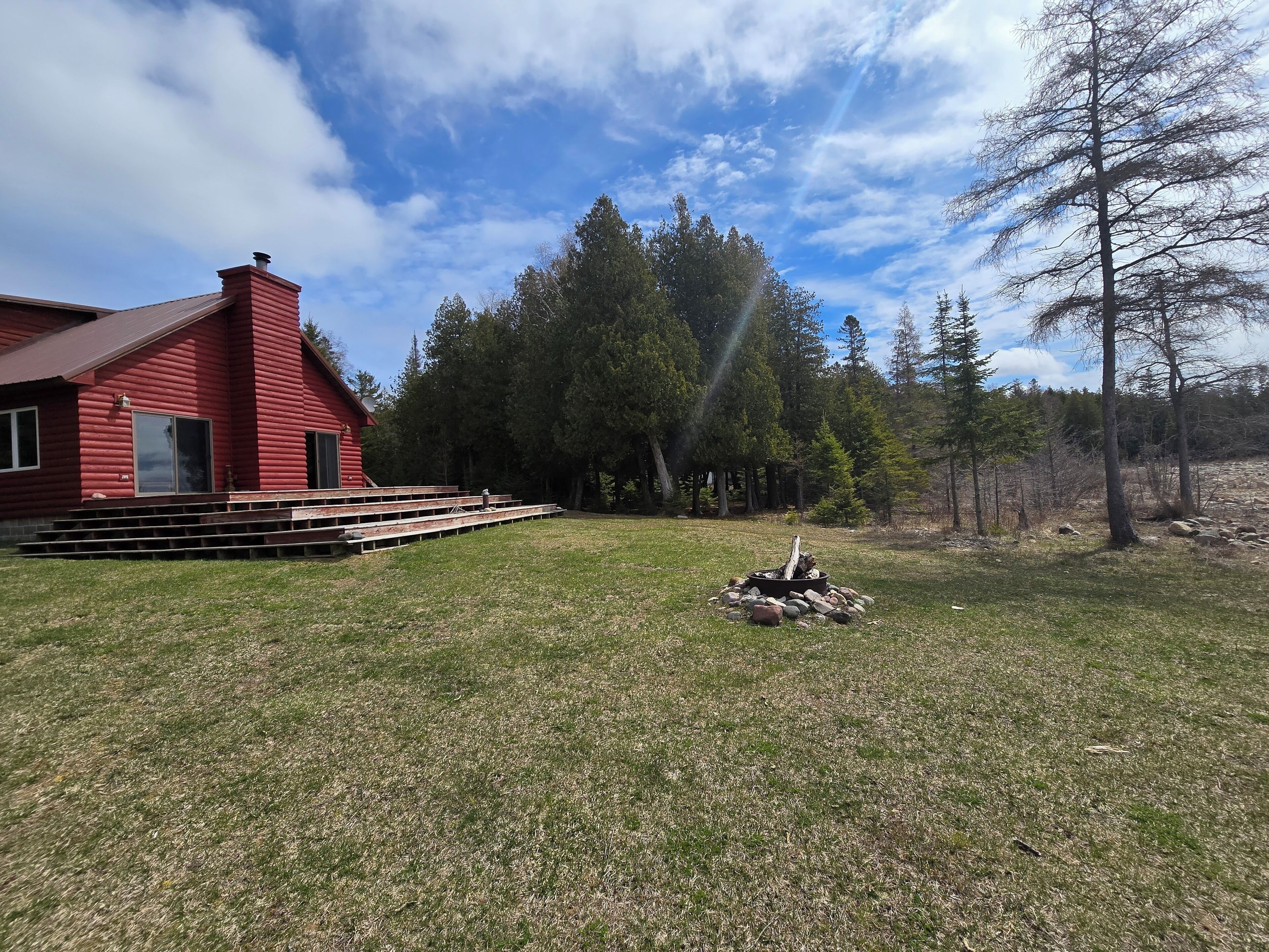 A red cabin with a fire pit in the yard, surrounded by trees.