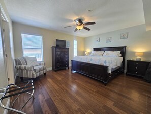 A bedroom with a bed, a chair, a dresser, a nightstand, a ceiling fan, and a window with blinds.