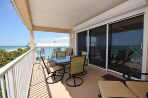 A balcony with a table and chairs, a sliding glass door, and a view of the ocean and a distant building.