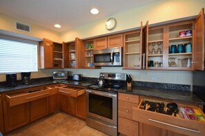 A kitchen with wooden cabinets, a microwave, an oven, and a clock on the wall.