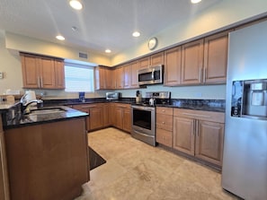 A kitchen with wooden cabinets, a stainless steel refrigerator, a microwave, a toaster, and an oven.