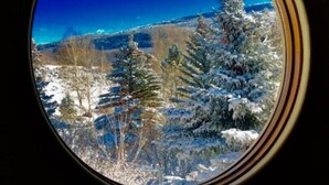Une fenêtre circulaire offrant une vue sur un paysage enneigé, avec des arbres et une montagne.