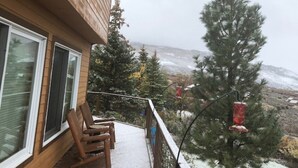 Une terrasse en bois avec deux chaises, une rambarde et une vue sur un paysage enneigé parsemé d’arbres.
