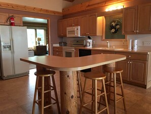 Uma cozinha com armários de madeira, uma ilha central com banquetas, micro-ondas e cafeteira.