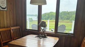 Puinen sisustus, jossa on suuri pöytä ja tuoleja, kyltti, jossa lukee ”JOHTOPORTAAN PÄÄMAJA”, ja suuret ikkunat, joista avautuu näkymä vehreään maisemaan.
