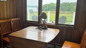 Un intérieur en bois avec une grande table et des chaises, une enseigne indiquant « POSTE DE COMMANDEMENT », et une vue sur un paysage verdoyant à travers de grandes fenêtres.
