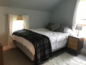 Ein Schlafzimmer mit einem Bett, einem Nachttisch, einer Lampe und einem Fenster mit Vorhängen.