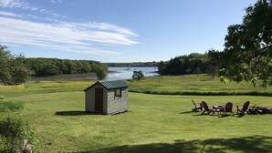 Pieni puinen mökki, jossa on metallikatto, nurmikenttä ja taustalla järvi.