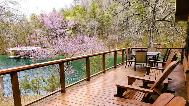 A wooden deck with a railing overlooking a body of water, surrounded by trees and a gazebo.