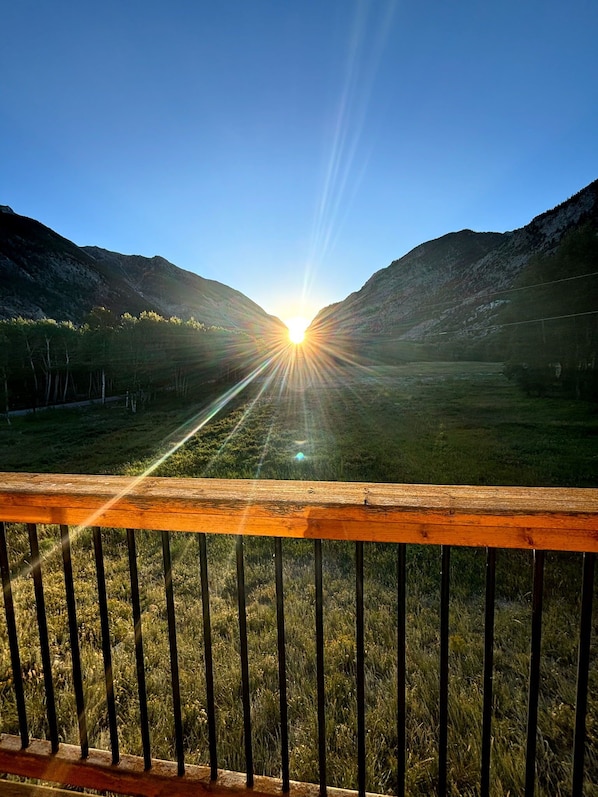 A wooden railing with a view of a sunlit valley and mountains.