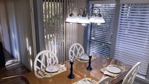 A dining area with a wooden table set for four, white chairs, and a window with blinds. - Newly Updated, Near Harbour Town 1st Floor 2 Bedroom 2Bath  Villa  (Hilton Head Island)