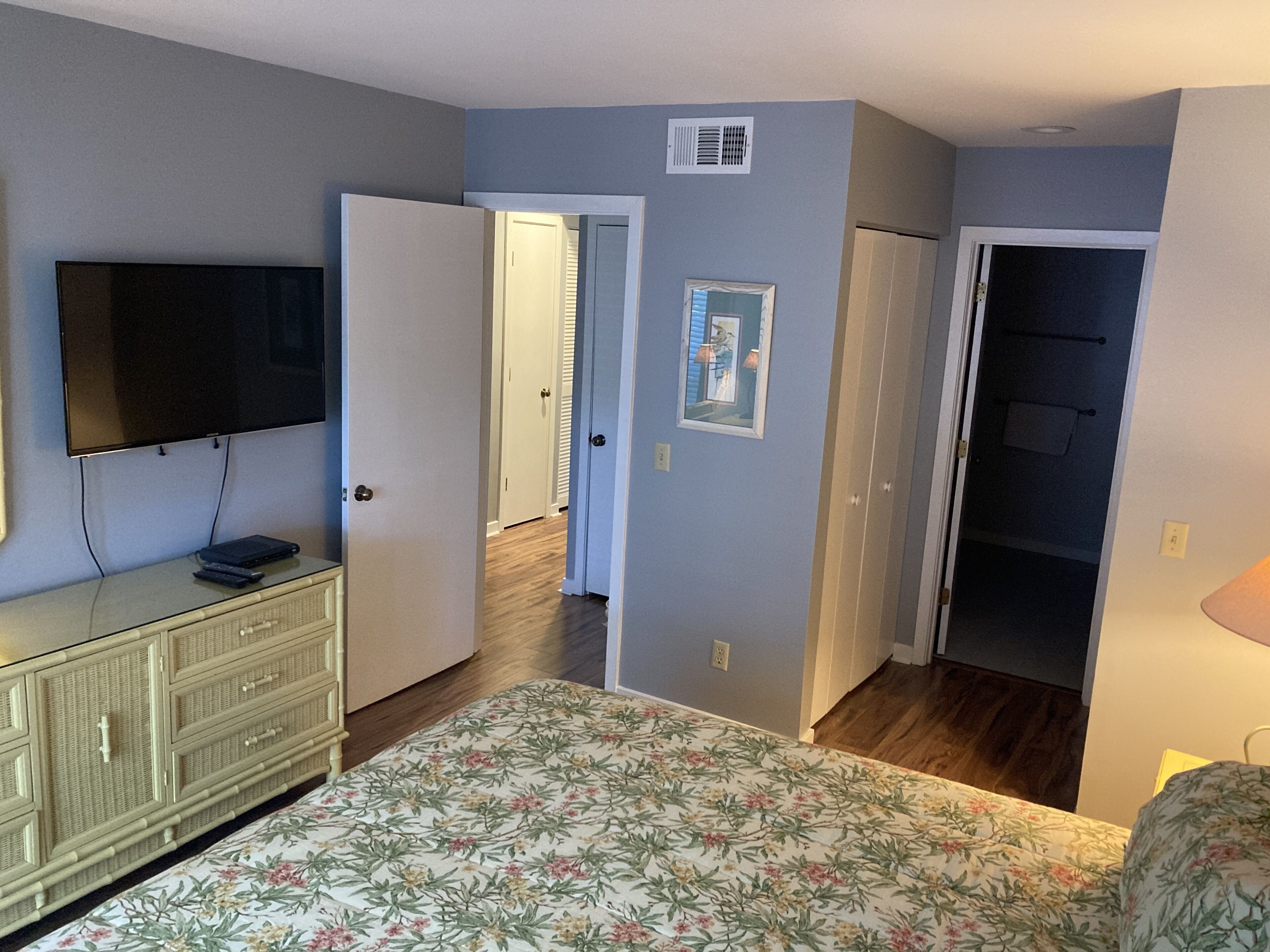 Un dormitorio con cama, cómoda, televisor y puerta que da a otra habitación.