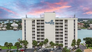 A multi-story hotel with balconies, a waterfront view, and a logo on the building. - SUN, SAND & SURF! (Pensacola)