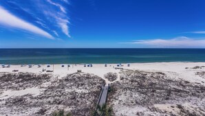 A beach with a long pier extending into the ocean, surrounded by white sand and sparse vegetation. - SUN, SAND & SURF! (Pensacola)