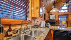 A kitchen with granite countertops, stainless steel sinks, wooden cabinets, a coffee maker, and a sign reading 'BROKEN BOW WILLY CABINS.'