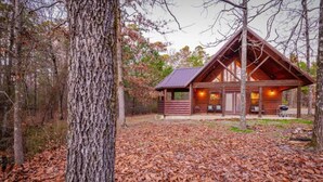 A cabin with a sloped roof, wooden exterior, and a porch with seating.