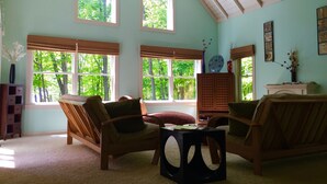 A cozy room with two large windows, a wooden ceiling, and a fireplace. - Lake Michigan Home on Tunnel of Trees with Game Room and Views (Harbor Springs)